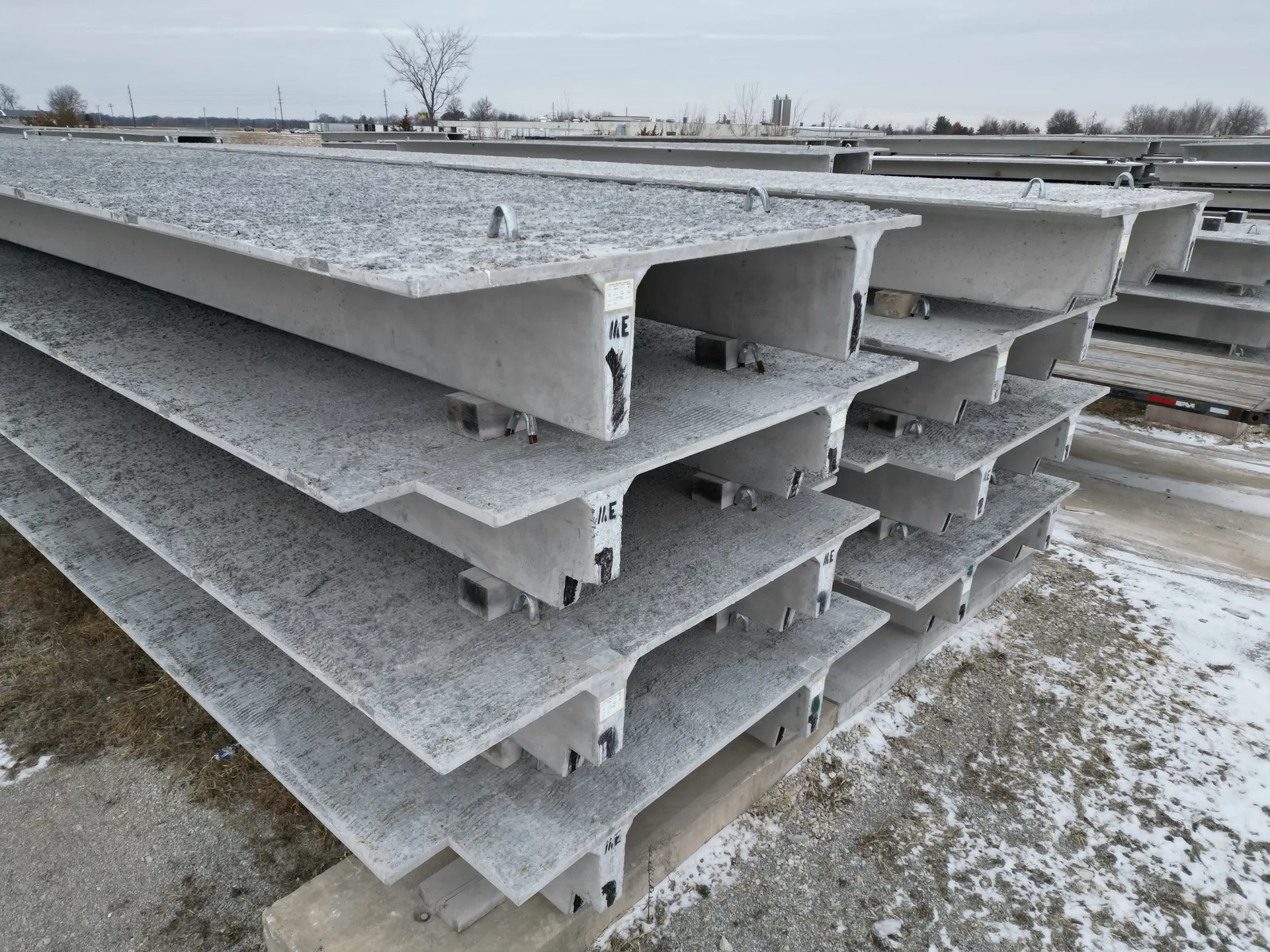 Aerial view of snow-dusted precast double-tee members stacked in a plant storage yard.