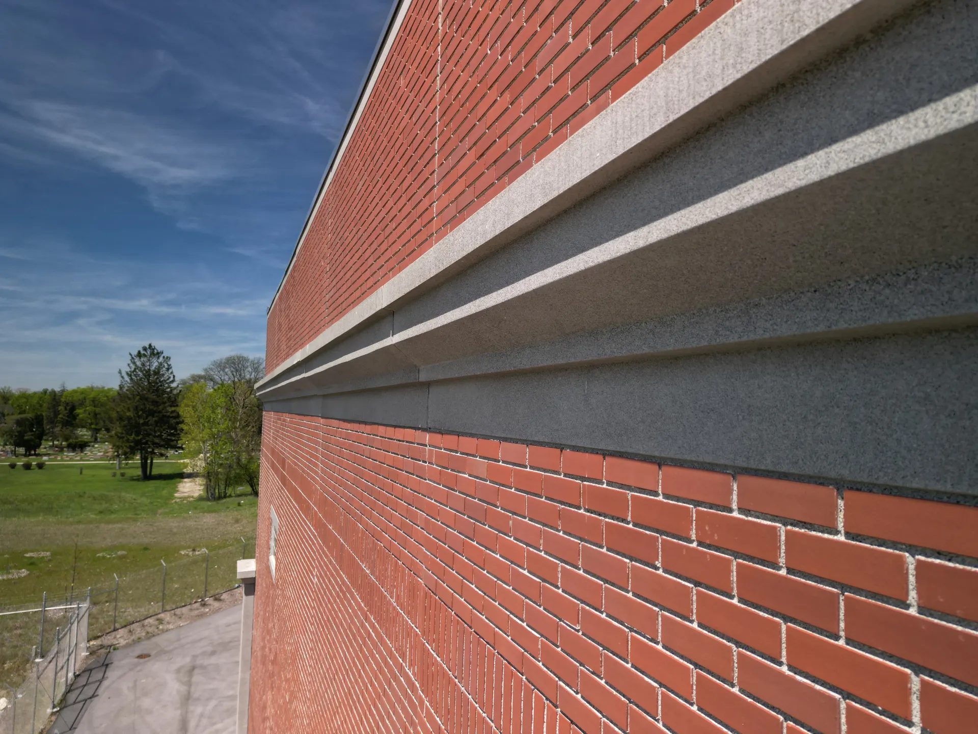 A finished thin-brick precast facade with cast stone banding, receding in strong perspective under a blue sky.