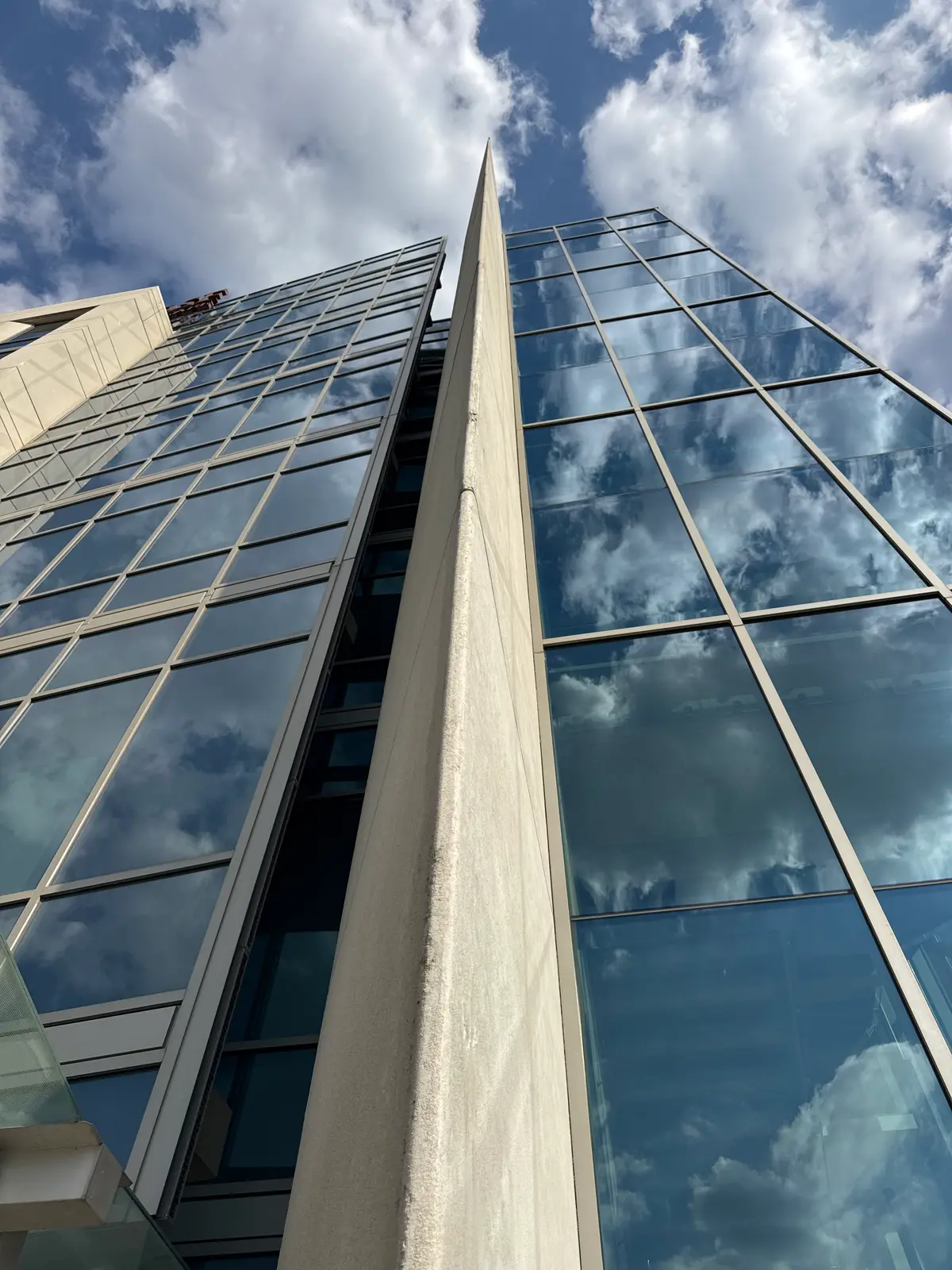Looking up the corner of a tower where a precast concrete fin meets a blue glass curtain wall.