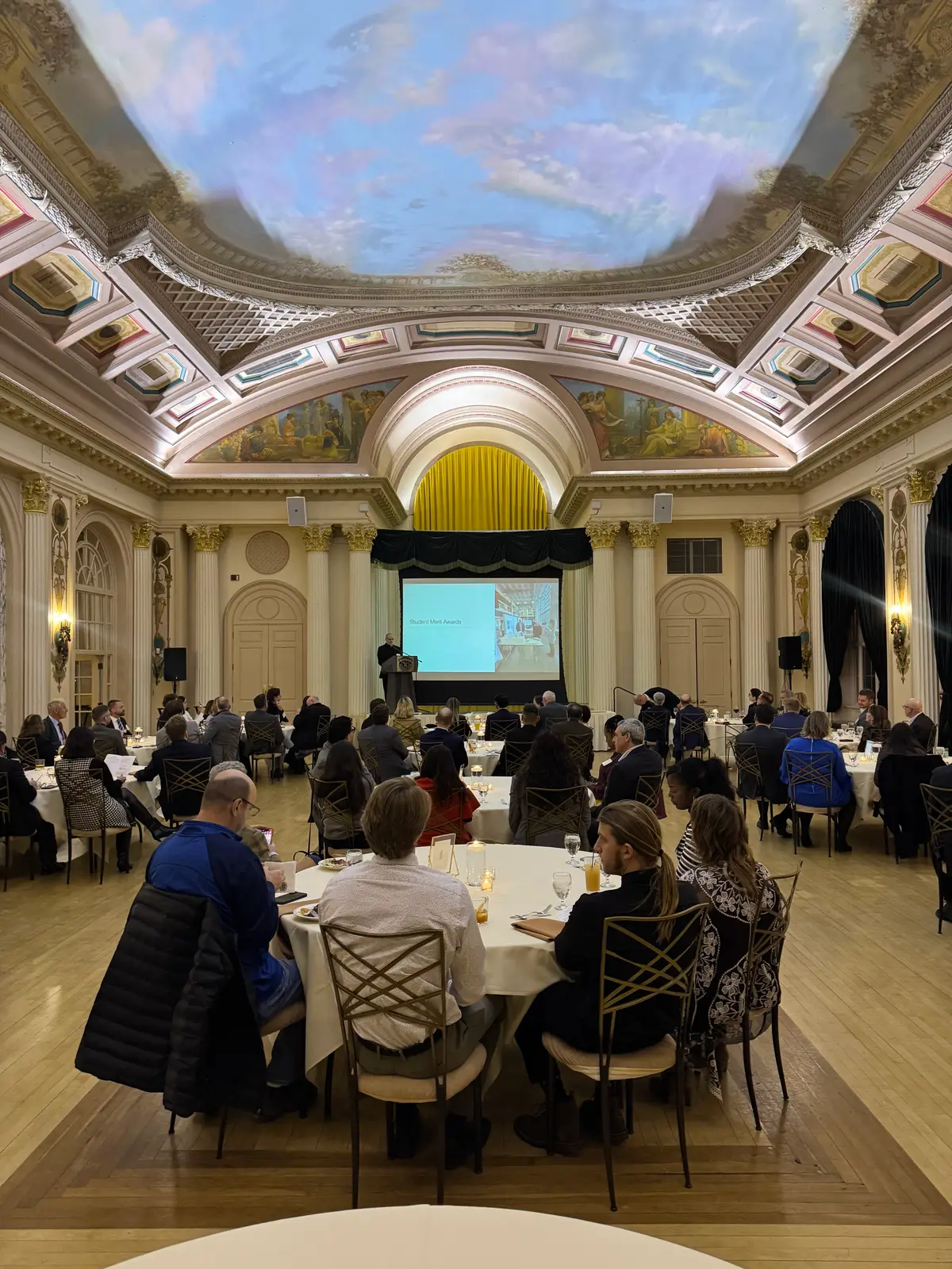 An association dinner in an ornate historic ballroom with a painted ceiling, seen from the back tables.