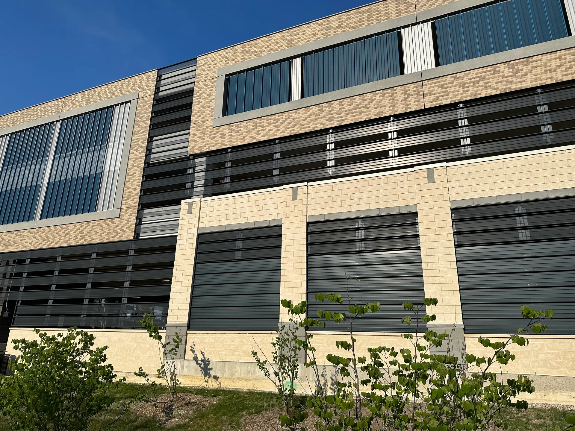 A finished building with tan brick, cast stone banding, and dark metal louvers under a clear sky.