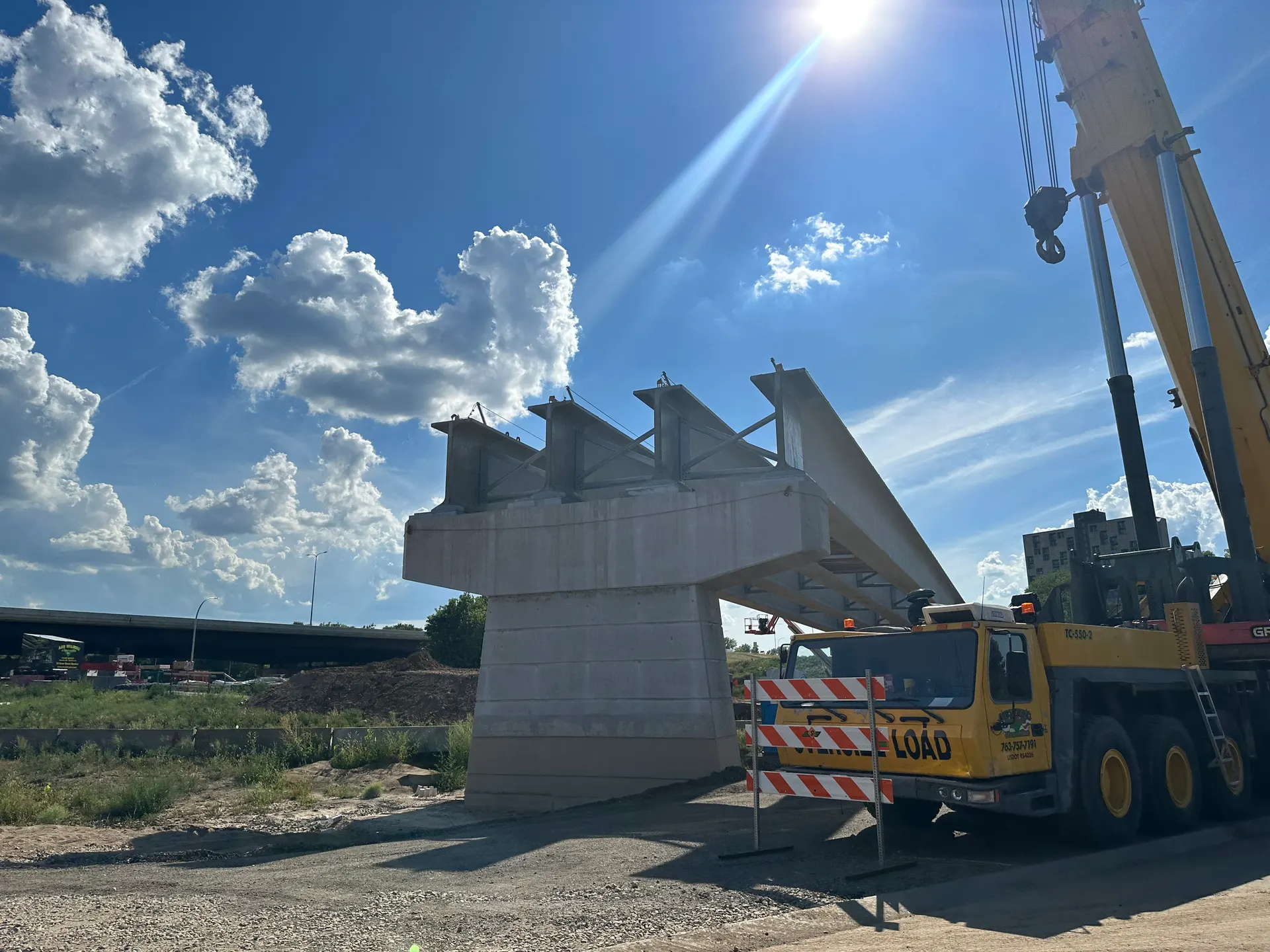 A mobile crane sets a precast concrete bridge girder onto a pier cap at a highway jobsite.