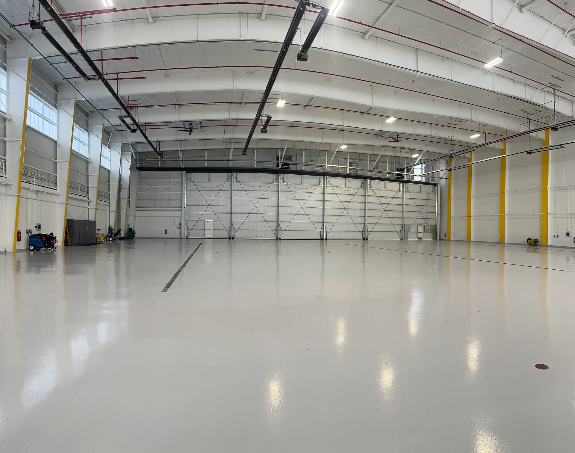 A large empty aircraft hangar with a freshly coated glossy floor and a full-width hangar door.