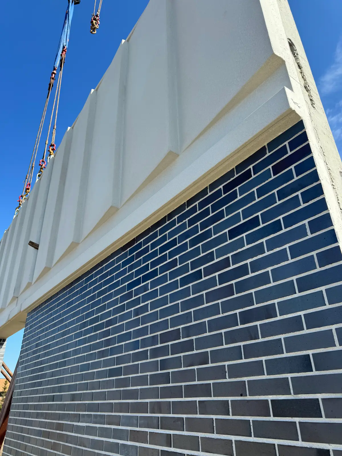 Detail of a precast panel mid-lift, dark thin brick below a white fluted band.