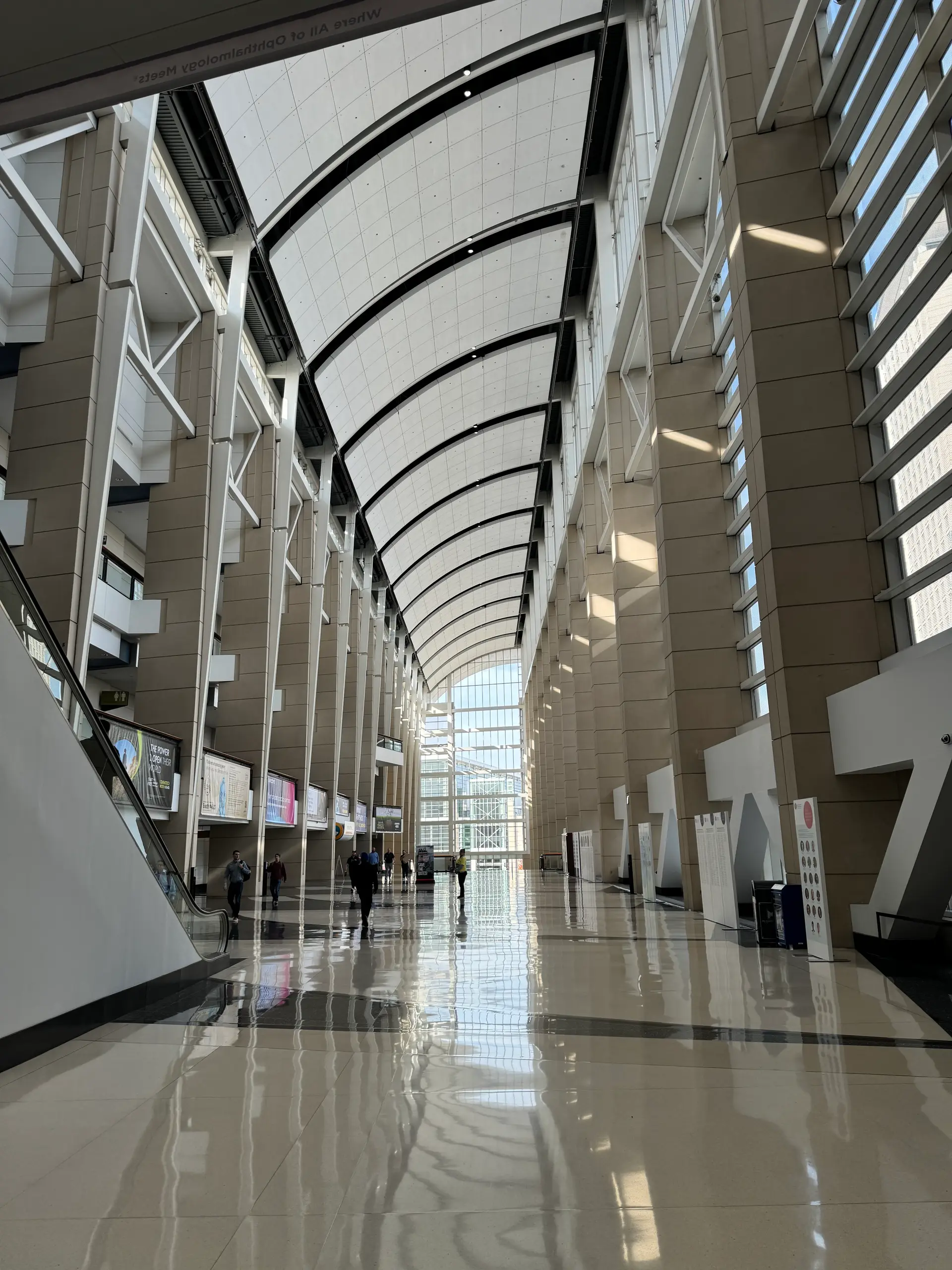 A soaring convention center concourse with a curved white ribbed ceiling and a tall glass wall.