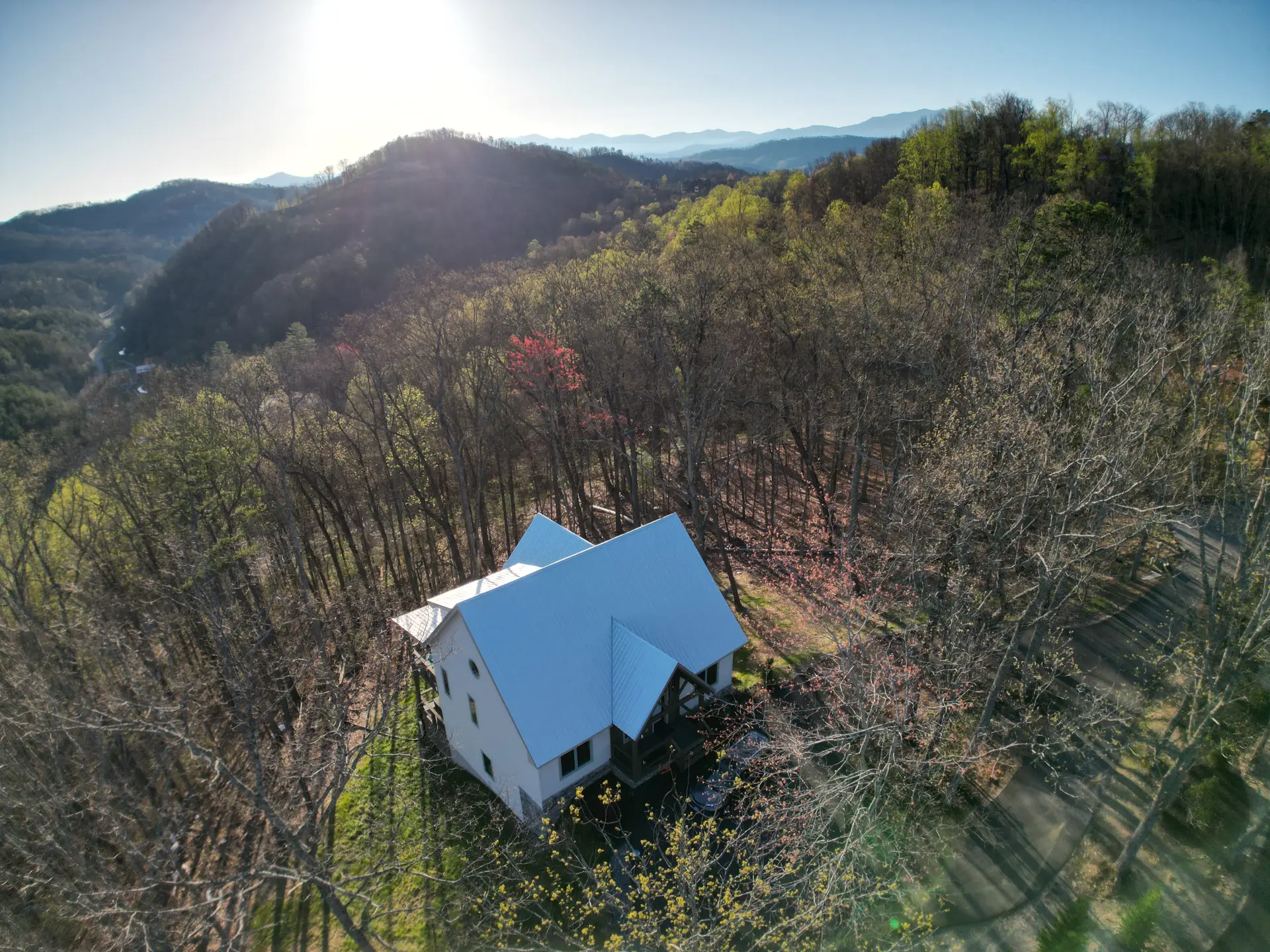 A newly built farmhouse-style home on a forested ridge with layered mountain ranges behind it.